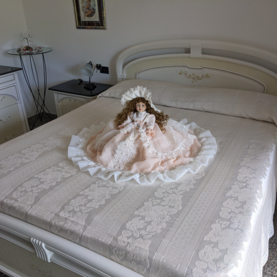 Bambola da letto modello "Beatrice" adagiata sul letto matrimoniale. Vista obliqua.