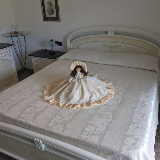Bambola da letto modello "Emma" adagiata sul letto matrimoniale. Vista obliqua.